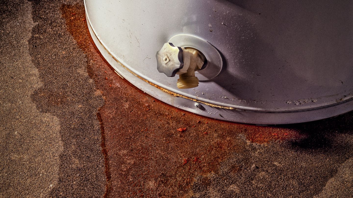 rusty leaking water heater with rust stains and water on ground