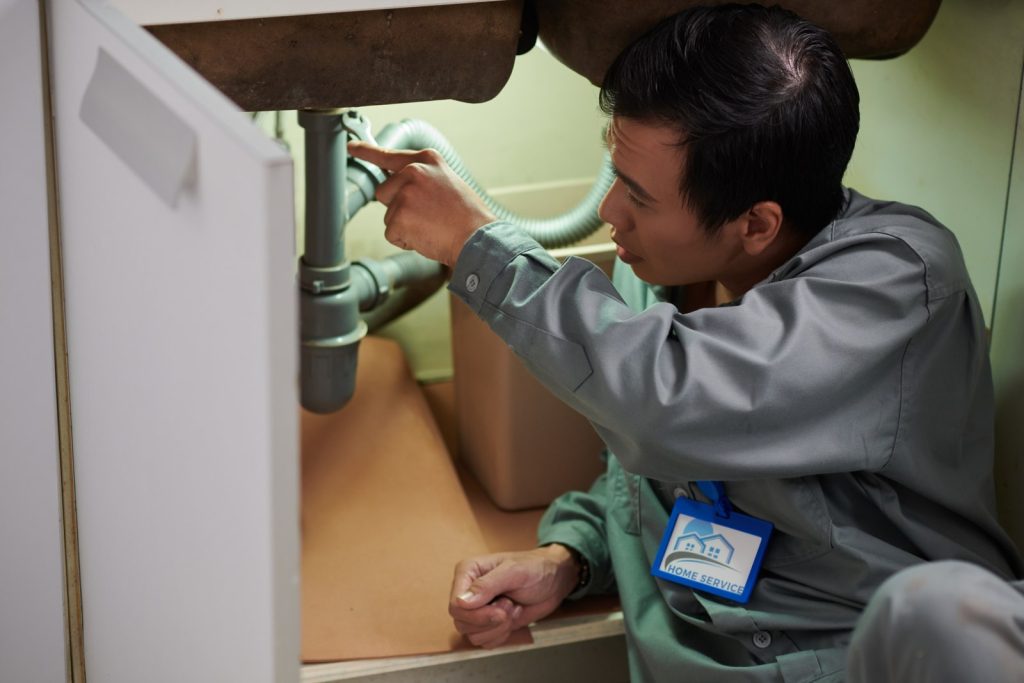 Home service technician inspecting pipes under a kitchen sink